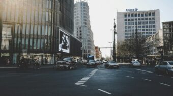 View of a street in Berlin city centre, showing a wide road with vehicles driving and tall buildings either side.
