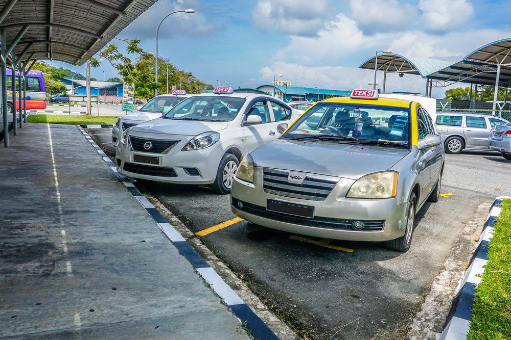 brunei-taxi Local Brunei taxis (silver or white with a yellow roof) parked side by side next to a curb.