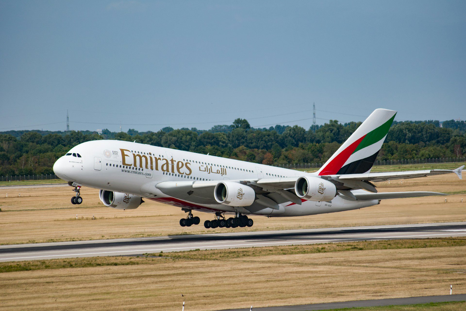 Emirates Airbus A380 lifting off from the runway at Dubai Airport, with landing gear still visible and desert-toned grass fields in the background, representing a typical scene of Dubai Airport departures on a clear day.