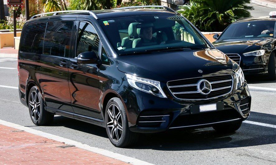 A black Mercedes minivan driving down a road lined with palms.