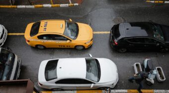 Top-down view of a yellow taxi, a black car, and a white sedan lined up on a rainy Istanbul street, with pedestrians walking nearby, capturing a typical urban scene for Uber Istanbul riders navigating busy city traffic.
