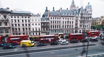 A London street filled with red double-decker buses, taxis, and cars, with buildings in the background.