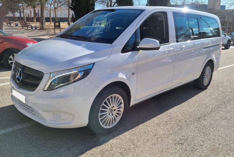 Side view of a white Madrid Airport taxi minibus, parked outside.