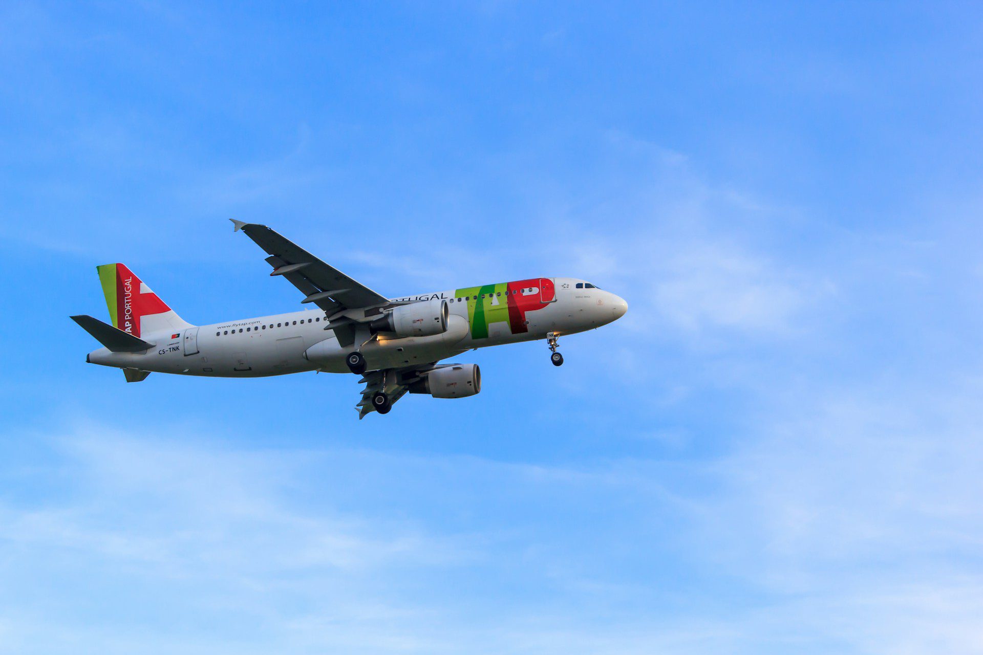 A TAP aeroplane flying through a blue sunny sky with a few scattered clouds.