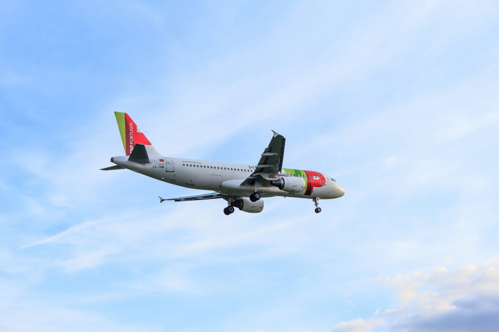 A TAP aircraft coming in for landing at Porto Airport against a blue and slightly cloudy sky.