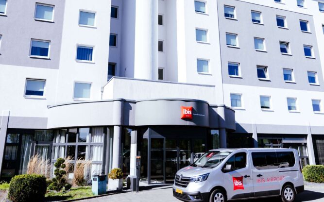 A photo of the exterior of the ibis hotel building near Luxembourg Airport, with the hotel's airport shuttle in close-up.