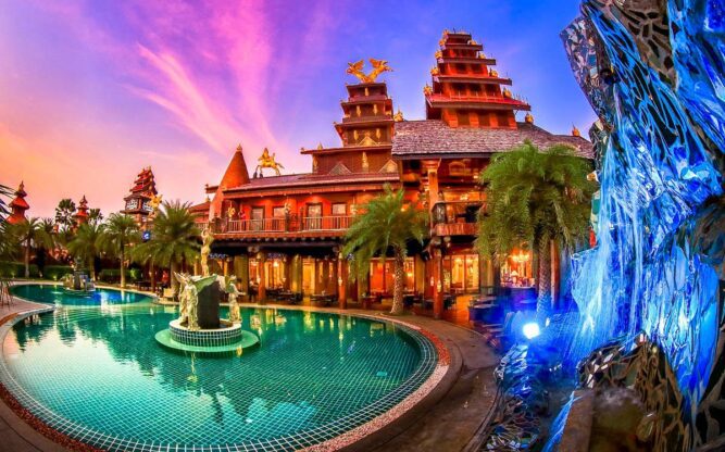 A view of the Ammata Lanta Hotel near Bangkok Airport with a turquoise pool in front and a blue ice-like sculpture to the right with exotic plants