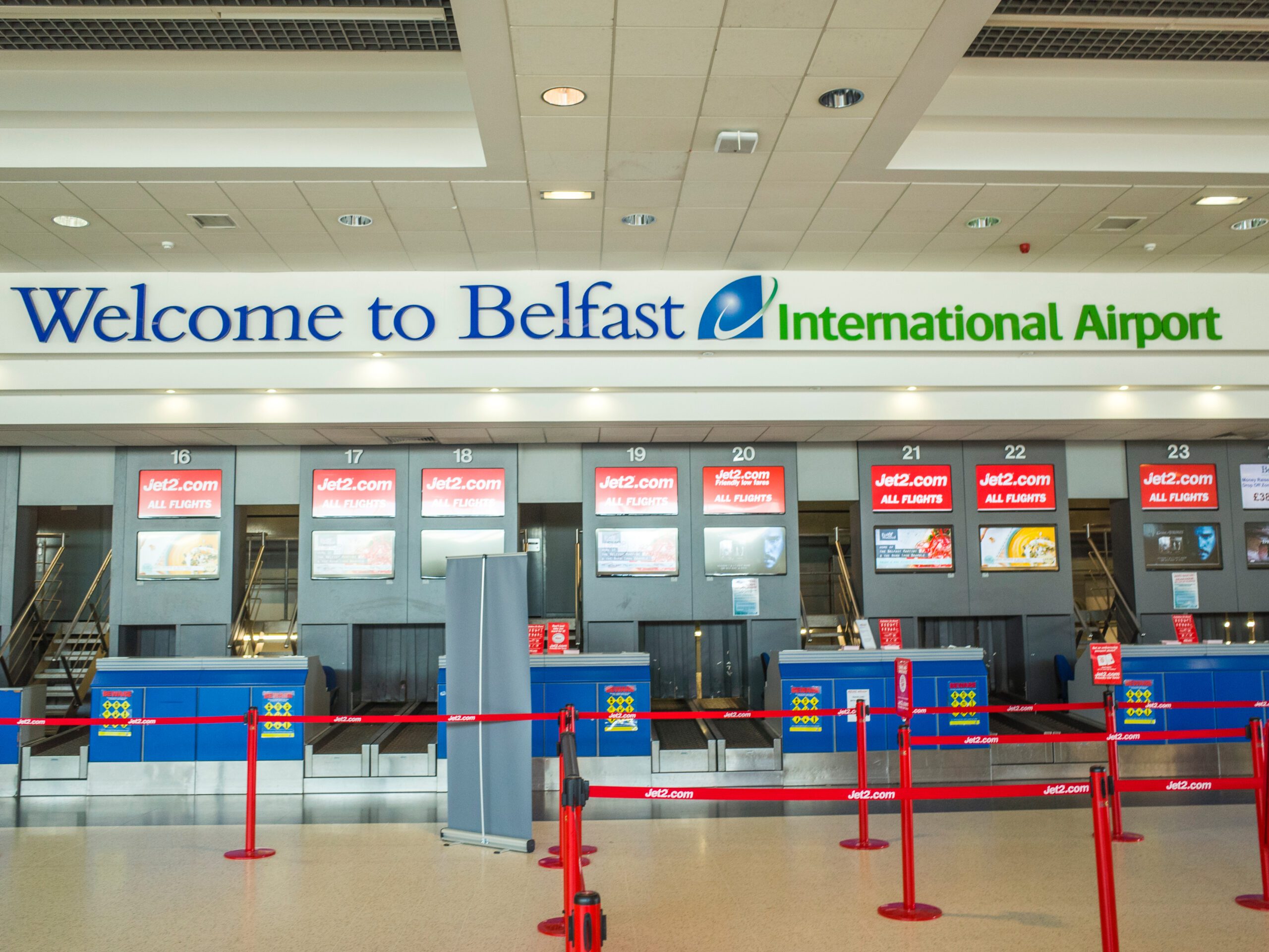 A photo taken just inside the Belfast International Airport showing a roped-off check-in line in front of the airline counters with a welcome sign above them.