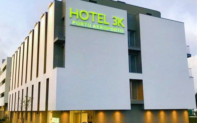 The white Hotel 3K Porto Airport Building with a green neon sign lit up on the roof.