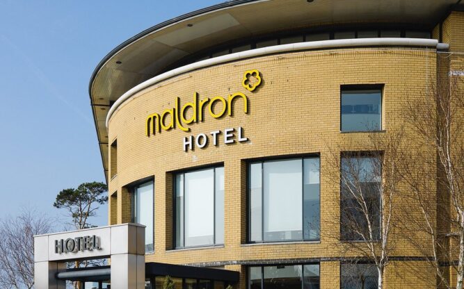 The yellow-brick front facade to the Maldron Hotel at Belfast International Airport with the hotel sign in yellow.