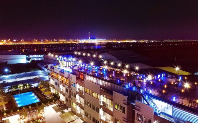 A view of the sky bar at the Suvarnabhumi Ville Airport Hotel at night with the Bangkok Airport runway in the background.