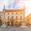 A beautiful plaza in Ravenna filled with sculpted pylons and pale yellow historic buildings with ornate windows and rounded archways.