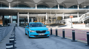 A blue Istanbul taxi approaches the entrance of Istanbul Airport under a large modern terminal canopy during daytime, offering convenient city transport for arriving travelers.