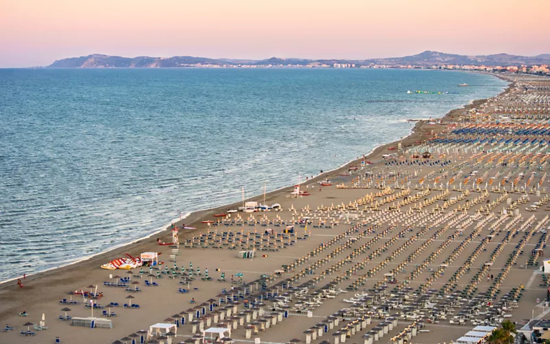 Hundreds of lounge chairs lined up in perfect rows on Rimini Beach looking out over the flat ocean.