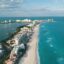 Aerial view of the coast of Cancun, with hotels lining the beach, and a body of water either side.