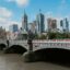 View of a bridge over a river in central Melbourne, with skyscrapers in the background and blue skies above.