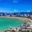 A sandy beach lined with houses and hotels against the backdrop of a blue sky.
