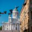 Fabric flags wave overhead in front of a white ornate building in Helsinki