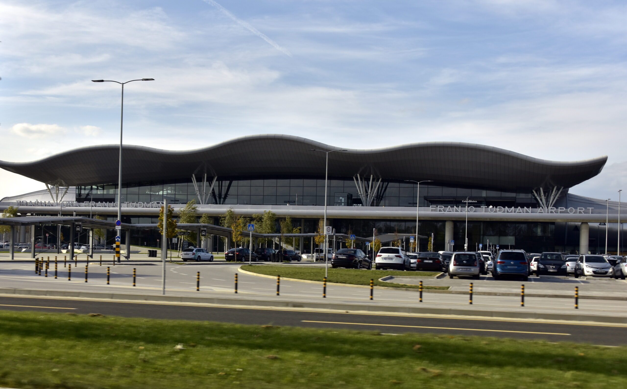 The front view of the Split Airport Terminal with a a road running along in front of it next to a grassy area.