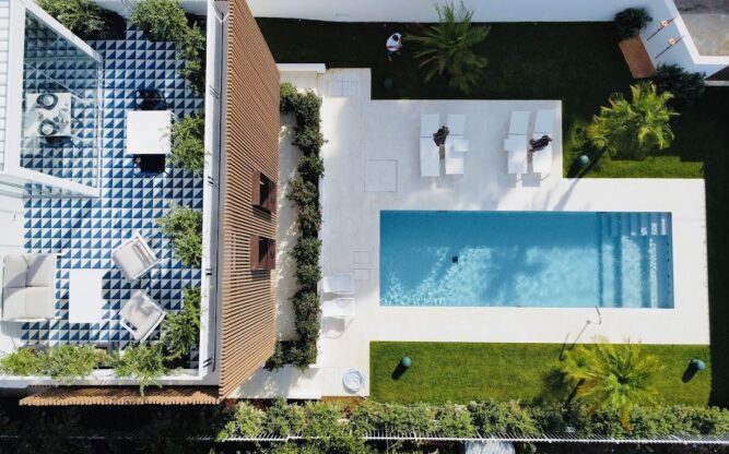 An aerial view of the Marina Boutique Rooms near Palermo Airport with a pool outlined with white tiles and a blue and white checkered balcony with white tables and chairs.