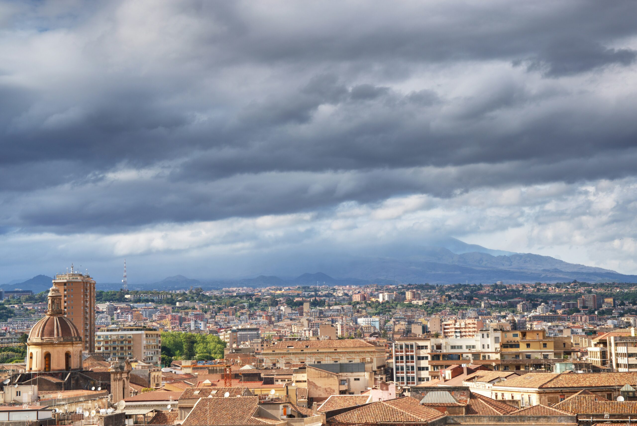 A view of a Catania city with lots of terracotta rooftops and a cloudy moody sky.