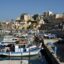 View of Heraklion city center on the water front, with small fishing boats docked at the port.