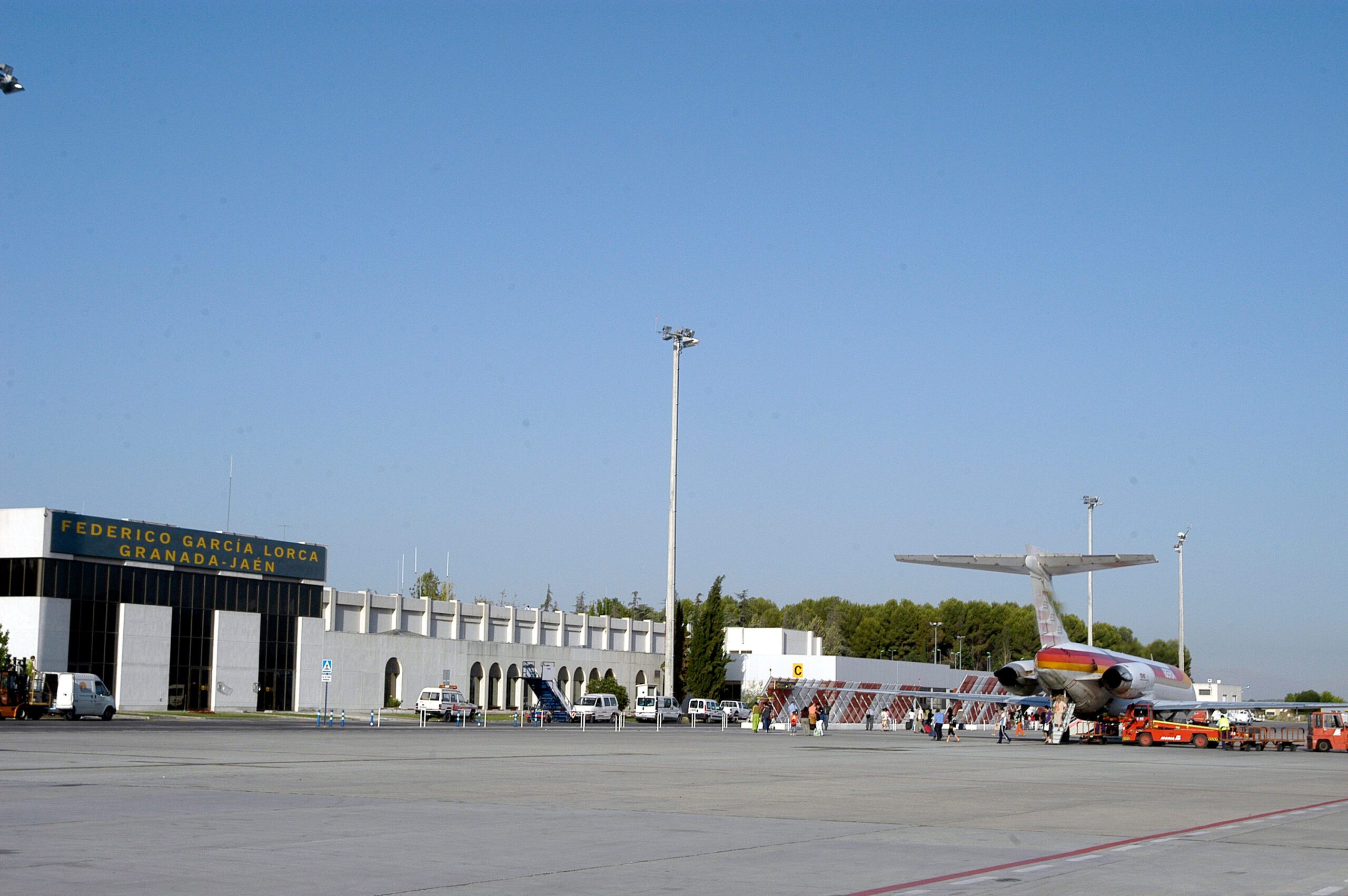 A front view of the main terminal building at Granada Airport, with a plane parked on the right side and blue skies above.