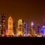 The Doha City skyline filled with sky-rise buildings lit up in neon colours at night.