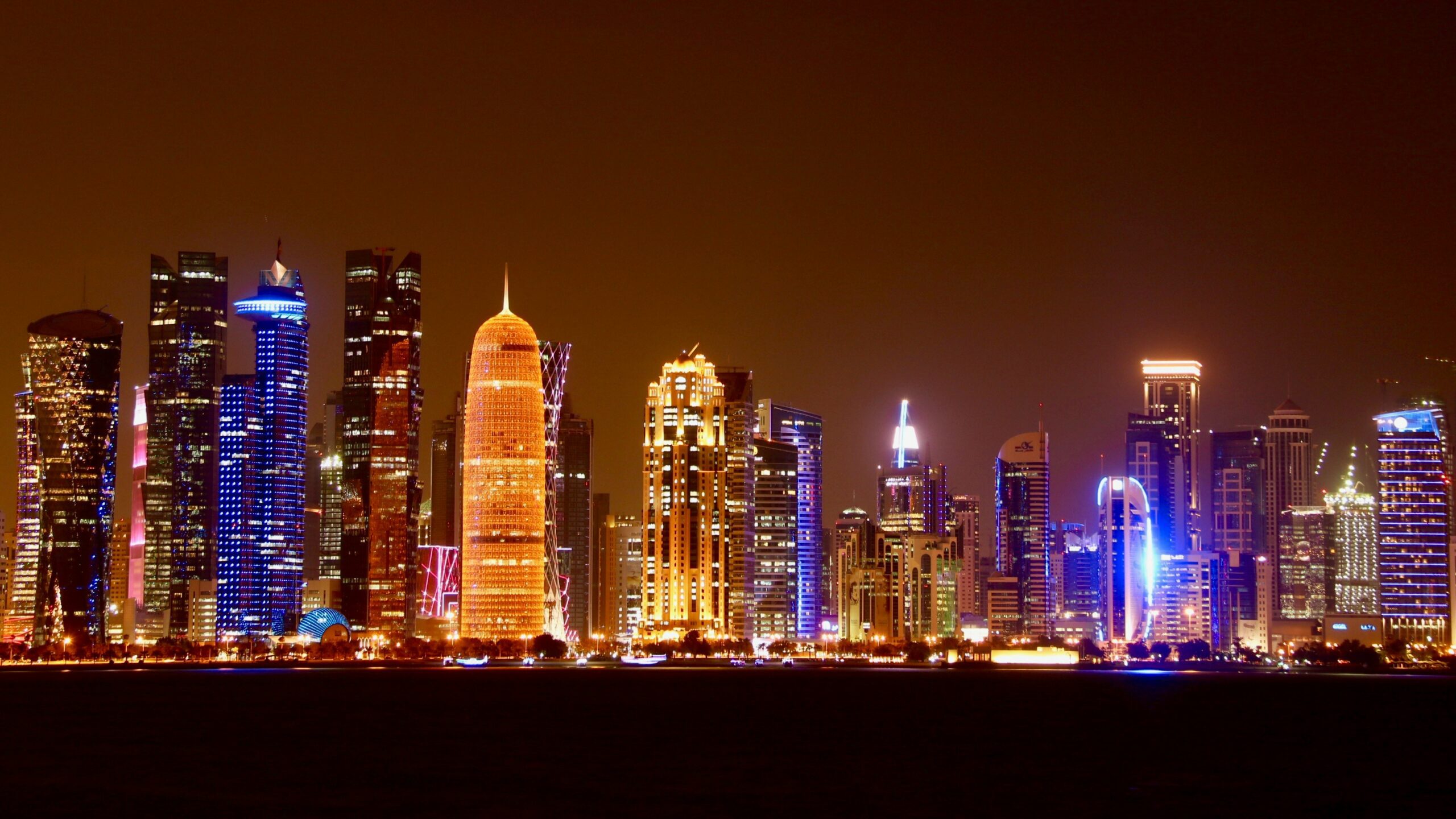 The Doha City skyline filled with sky-rise buildings lit up in neon colours at night.