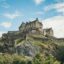 A large castle on top of a grassy hill in Edinburgh.