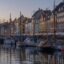 A row of colourful houses along the edge of a port with boats moored in the water.