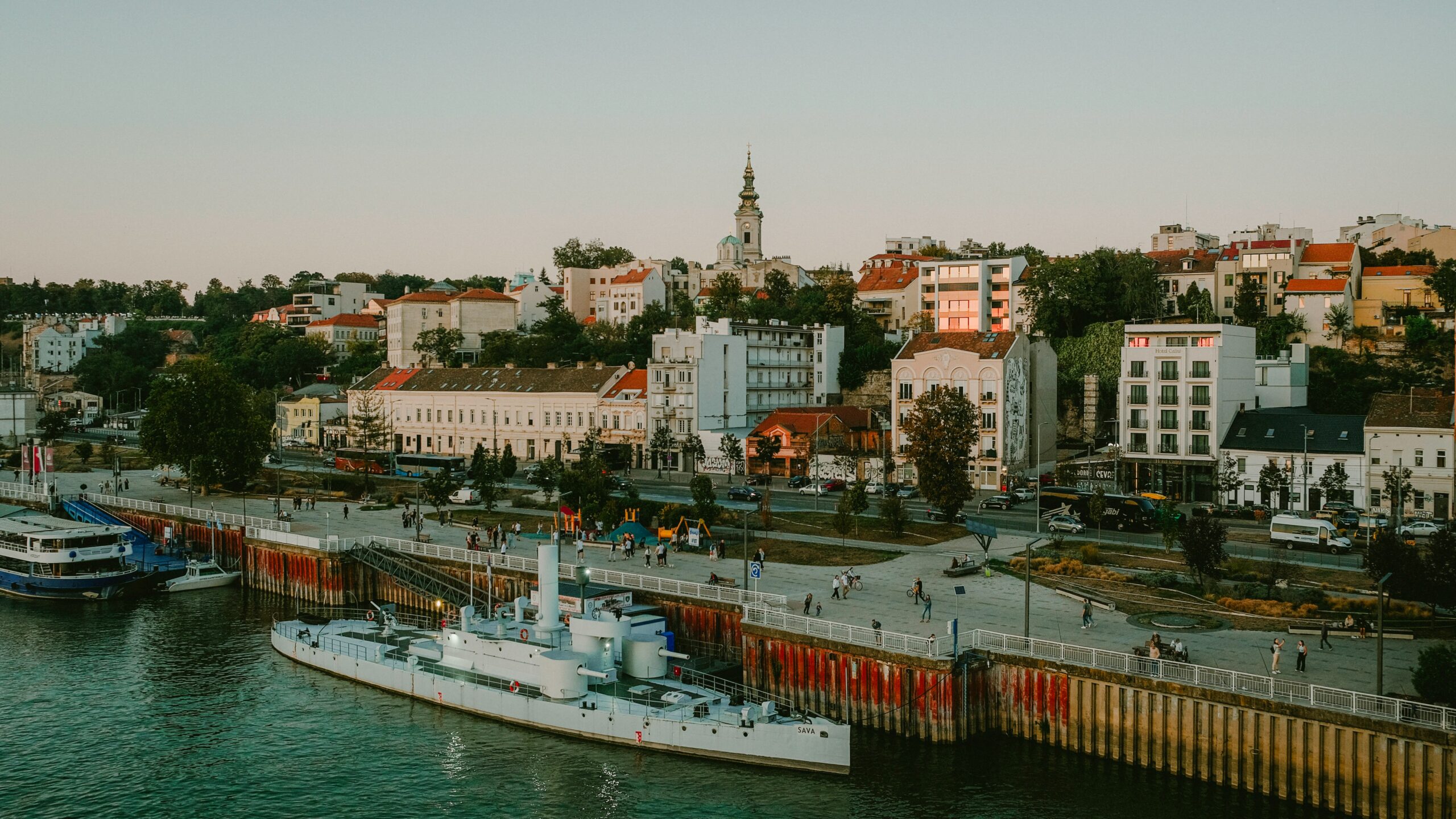 A boat sailing cruising past the shores of Belgrade city with lots of buildings and houses.