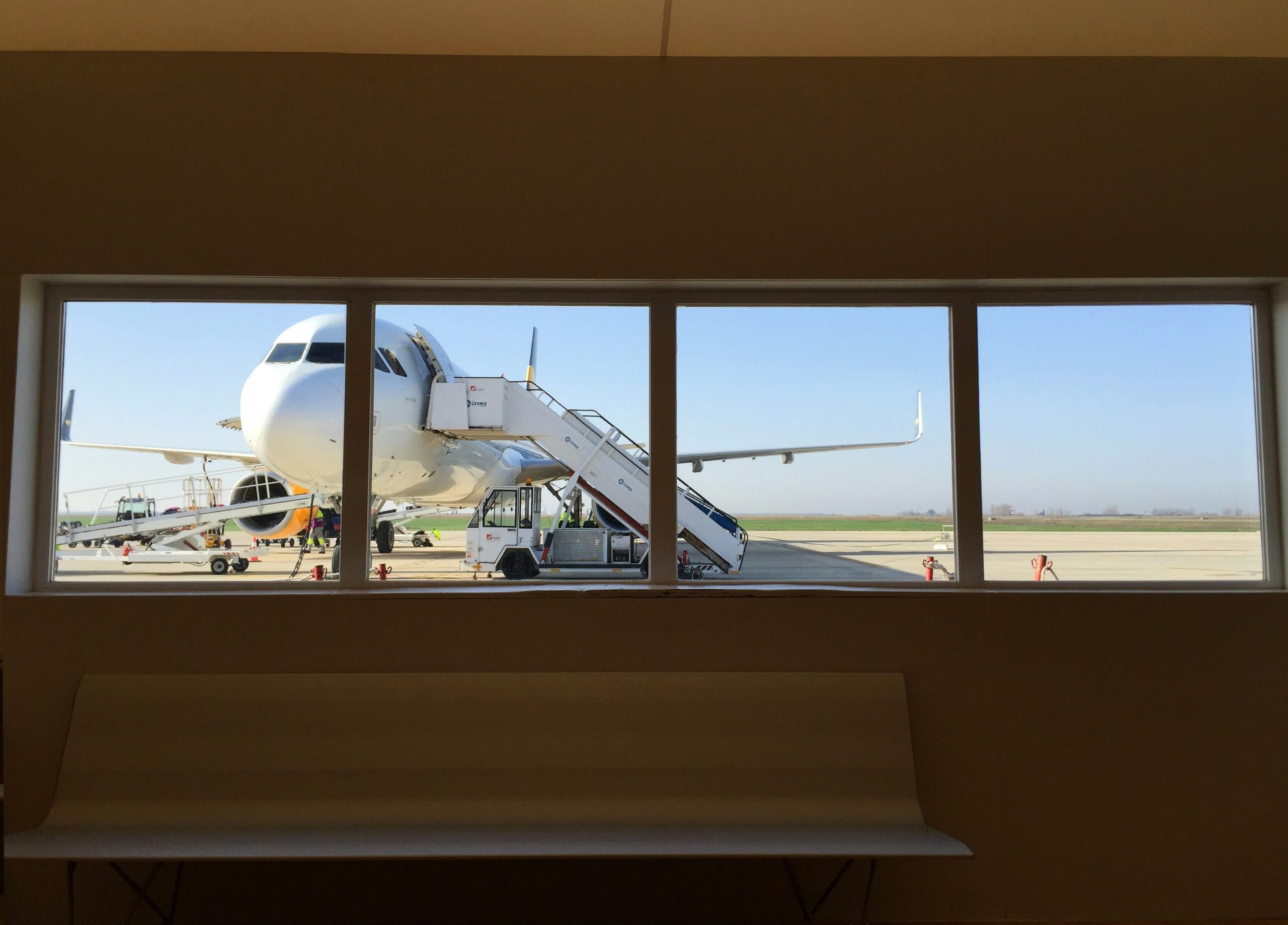The view of an aeroplane with a staircase leading to it through a window at Palermo Airport terminal