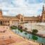 View of a park in central Seville, with terracotta buildings and a body of water with a bridge.