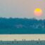 The sun is half pink and half yellow over the trees and shores of Vientiane