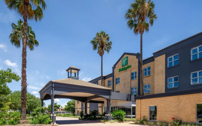 The driveway to the Holiday Inn at Johannesburg Airport on a sunny day with four palm trees in front.