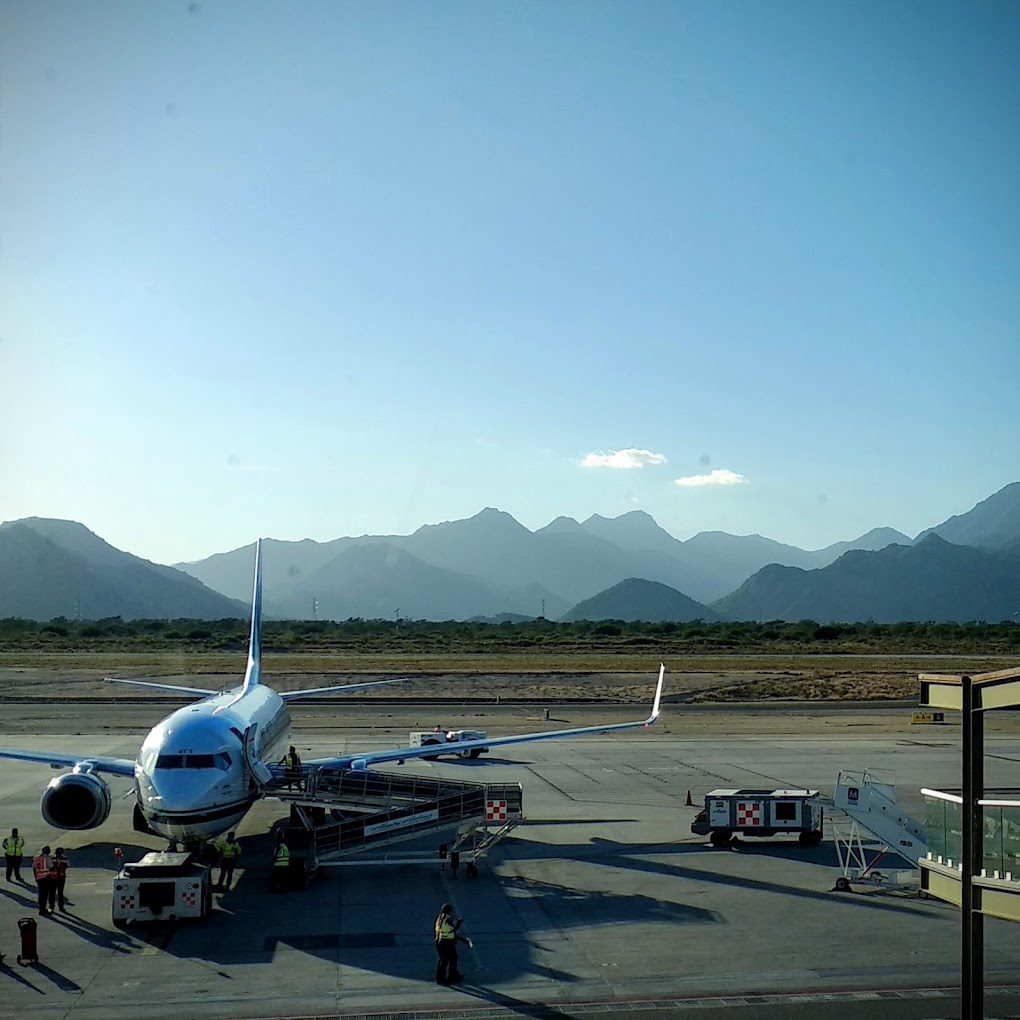 foggy mountains lay behind the plane tarmac with a parked plane at Los Cabos Airport