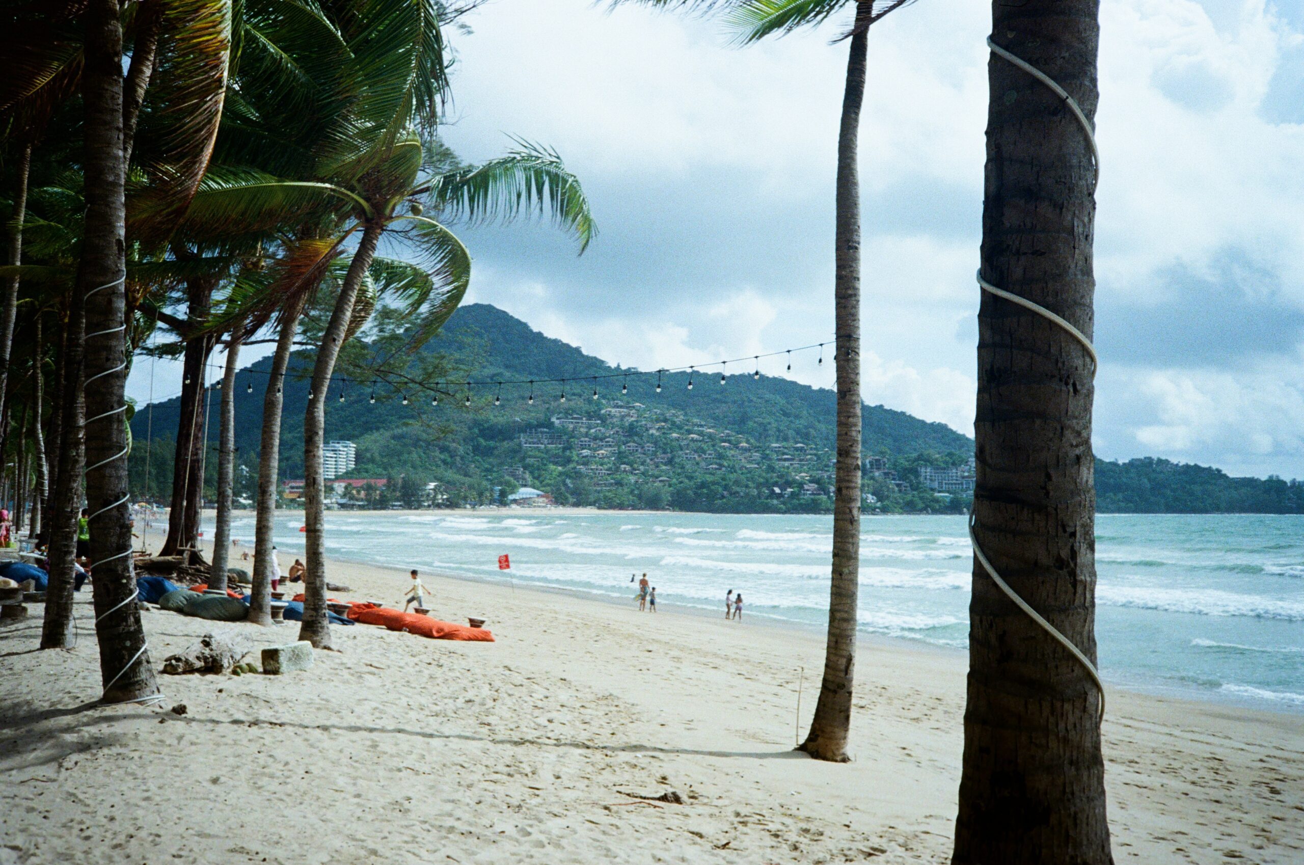 sandy beach with palm trees and mountains in the background in Phuket