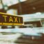A yellow taxi sign on the roof of an airport taxi.