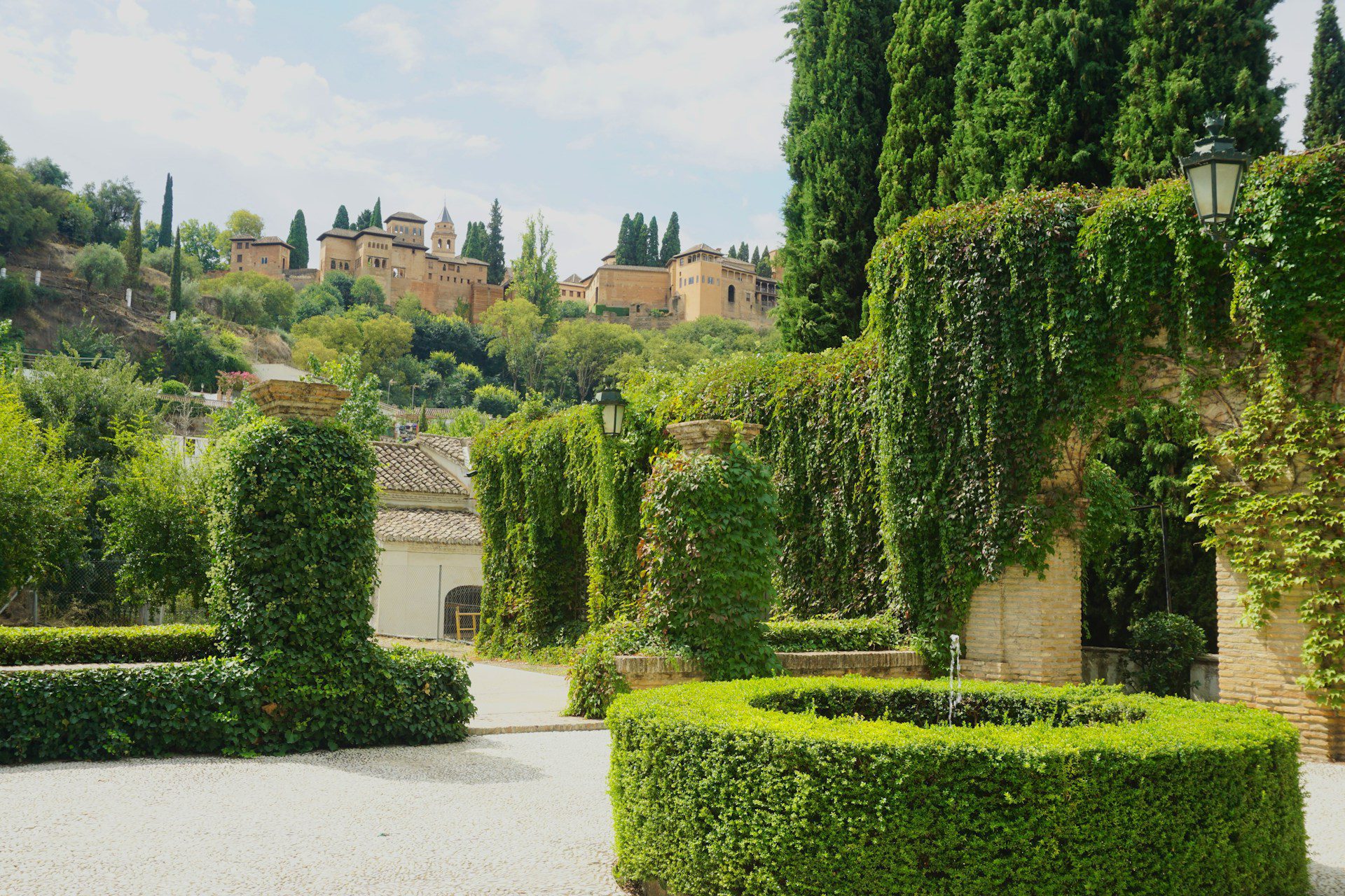 A view of the Alhambra on a hilltop in Granada, with sculpted trees and bushes in the foreground.