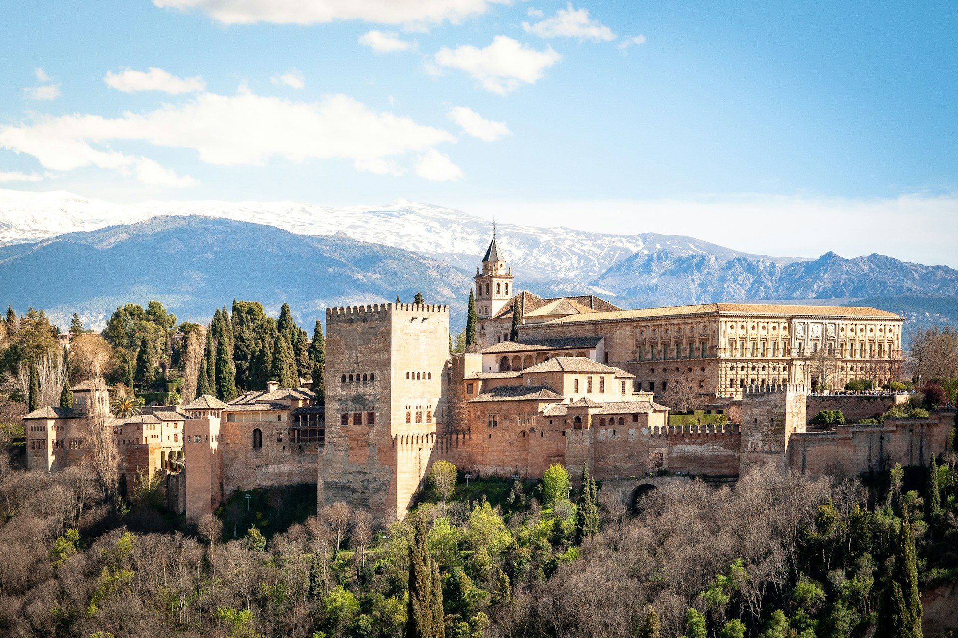 A view of the Alhambra in central Granada,with blue skies above and mountains in the background.