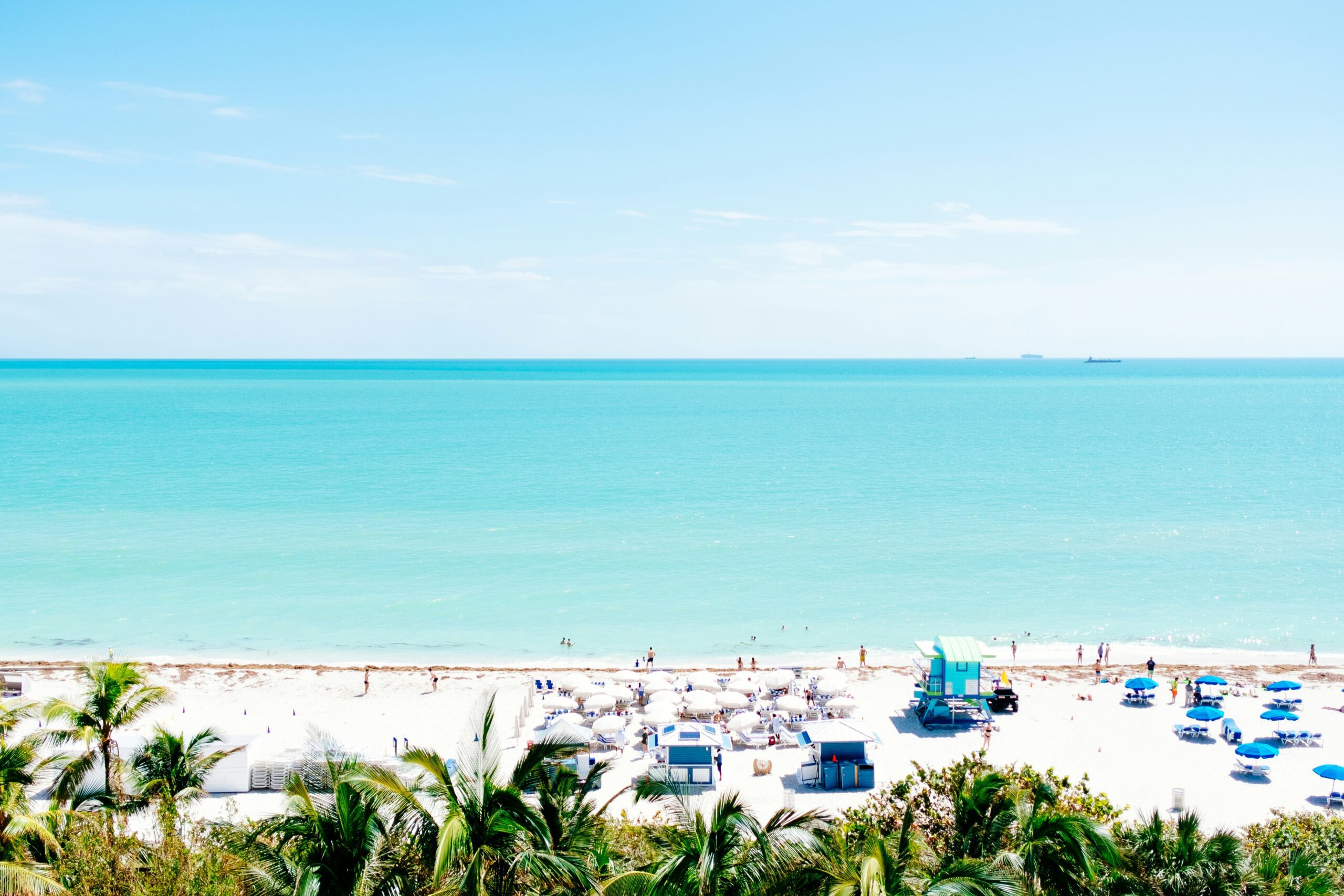 A beach with white sand, turquoise, palm trees and lots of people laying on the sand.