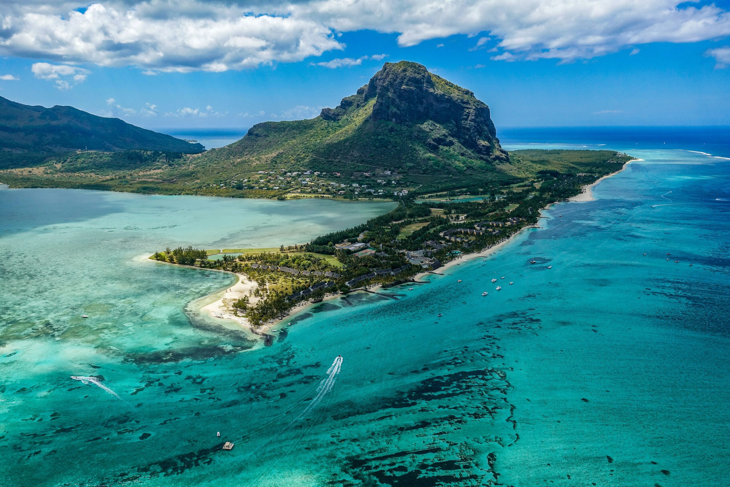 blue and green waters of Mauritius with a tall peak and jetty covered in greenery under a bright blue sky