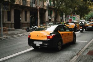 A black and yellow Barcelona taxi driving on a road in central Barcelona.