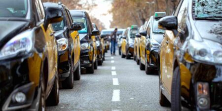 Two lines of yellow and black Barcelona taxis lined up in the road.
