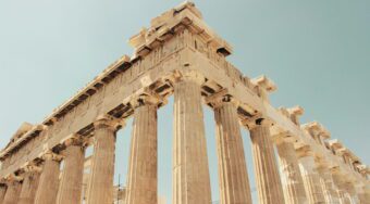 A photo looking up at the Acropolis from above, with multiple large columns and blue skies above.
