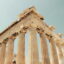 A photo looking up at the Acropolis from above, with multiple large columns and blue skies above.