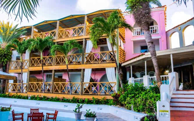 The pink facade and pool of Antigua's Ocean Point Resort and spa is framed by palm trees.