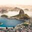 A city on the edge of the ocean with large pointed islands coming up out of the water with a setting sky in the background.