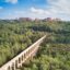 View of beautiful bridge cutting through lush trees and landscapes, with a city on the hill up ahead.
